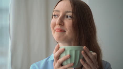 Portrait-Of-Happy-Woman-Looking-Out-The-Window-At-Home-While-Having-A-Cup-Of-Coffee