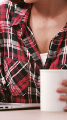 sección media de una mujer usando una computadora portátil mientras bebe café