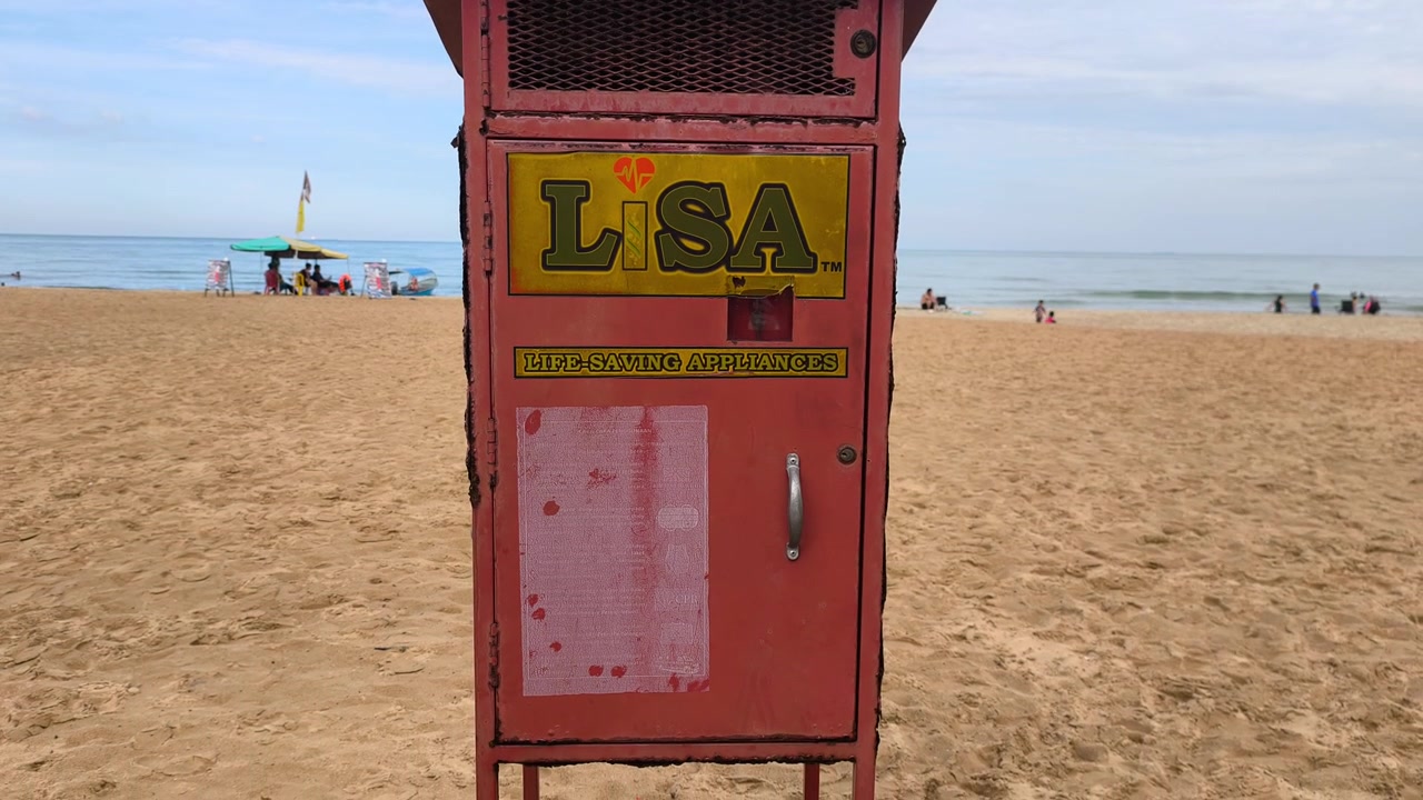 Una cassetta rossa brillante per attrezzature di salvataggio di emergenza posizionata su una spiaggia. Essenziale per la sicurezza in acqua e per rapide operazioni di salvataggio da parte dei bagnini o del pubblico. Progettata per un'alta visibilità durante le emergenze.