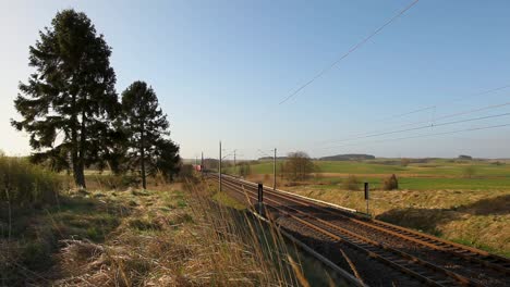 Tren-De-Carga-Rojo-Deutsche-Bahn-Moviéndose-A-Través-Del-Paisaje-Rural-En-Un-Día-Soleado,-Cielo-Despejado-En-El-Fondo