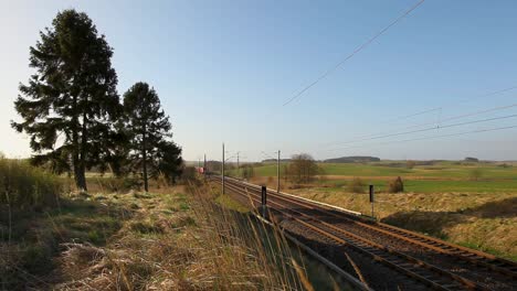 Red Deutsche Bahn freight train moving through rural landscape on sunny day, clear sky in background
