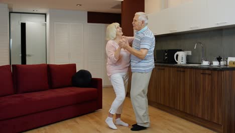 Senior-mature-couple-dancing-together-in-kitchen-at-comfortable-home-in-lockdown-for-coronavirus