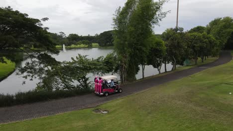 aerial shot following golfer and caddy on driving golf car at golf course