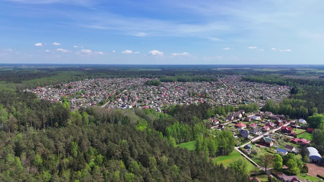 una pequeña ciudad rodeada de denso bosque bajo un claro cielo azul, vista aérea