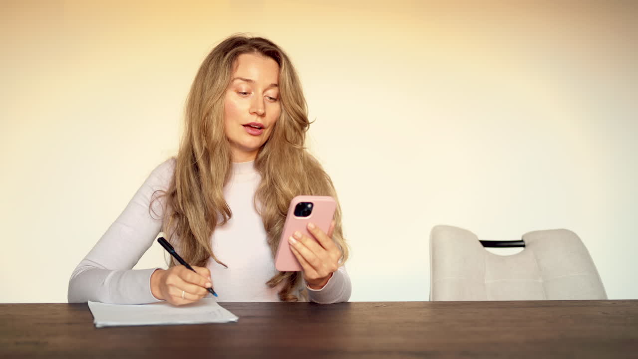 Woman talking on video call on the phone while holding a pen at a table