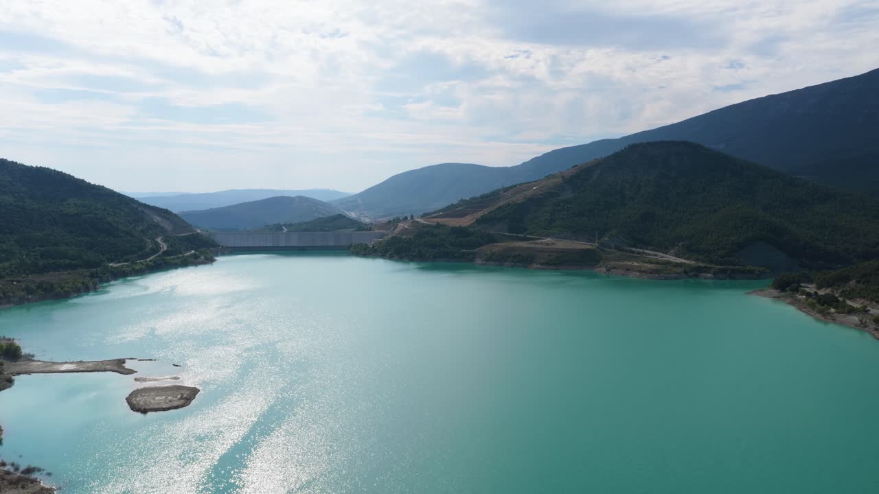 Veduta aerea di un bacino idrico turchese e una diga in un paesaggio montuoso