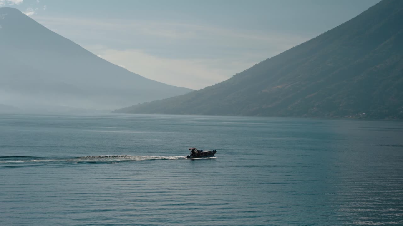 Küçük bir tekne, uzakta volkanların bulunduğu Atitlán Gölü'nde hareket ediyor