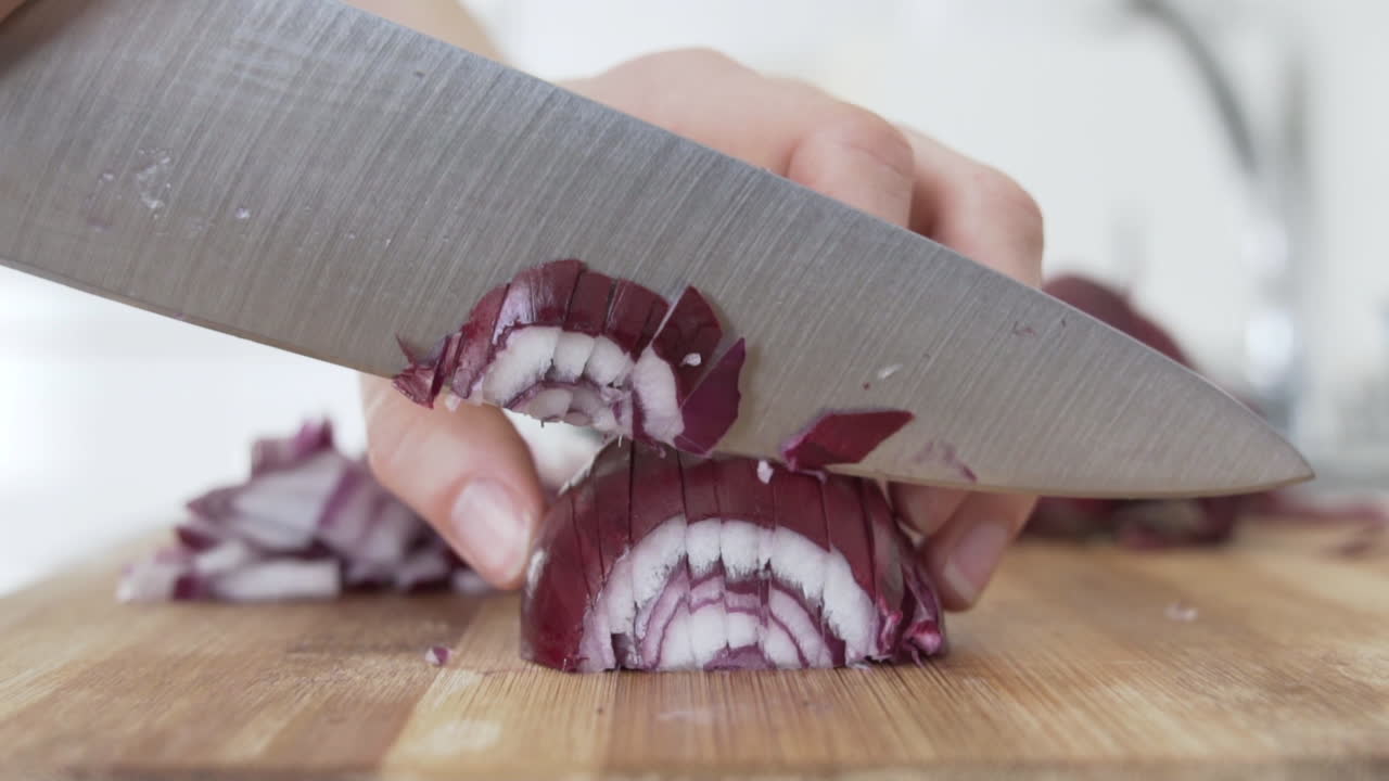 Close side view as chopping up, cutting red onion in the kitchen