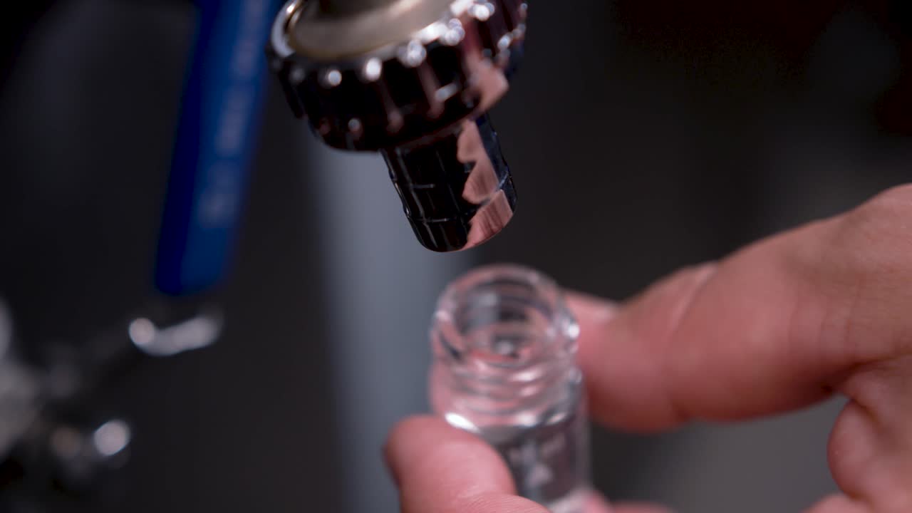 A person in a waterworks holds a small bottle in their hand, water is poured in and a sample is taken to check the water quality