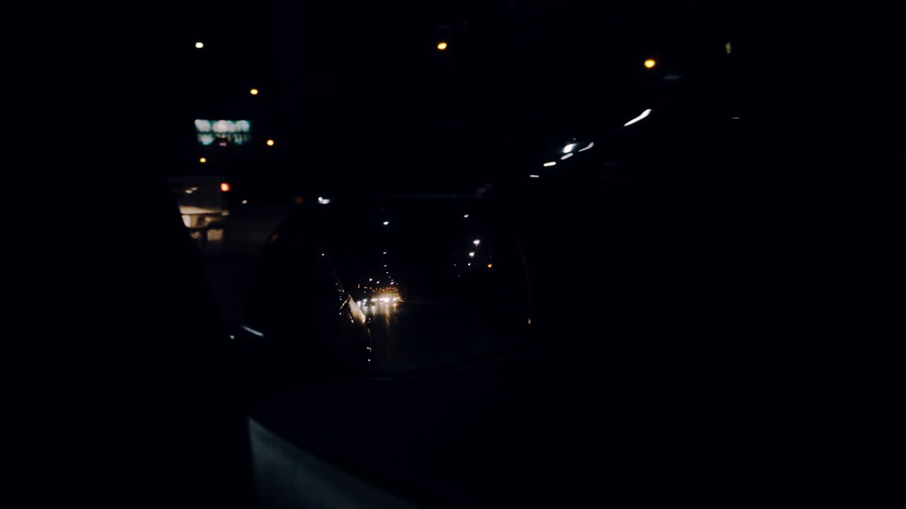 La luce dei fari dell'auto si riflette nello specchietto laterale.