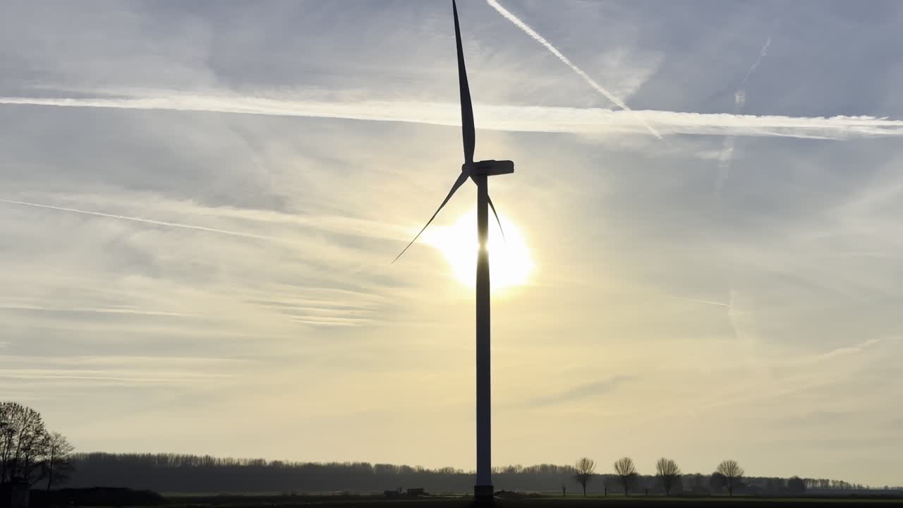 En moderne vindturbin sett i silhuett mot en lav sol. Baklys skaper en rolig, atmosfærisk scene som symboliserer fornybar energi, ren energi og en bærekraftig fremtid.