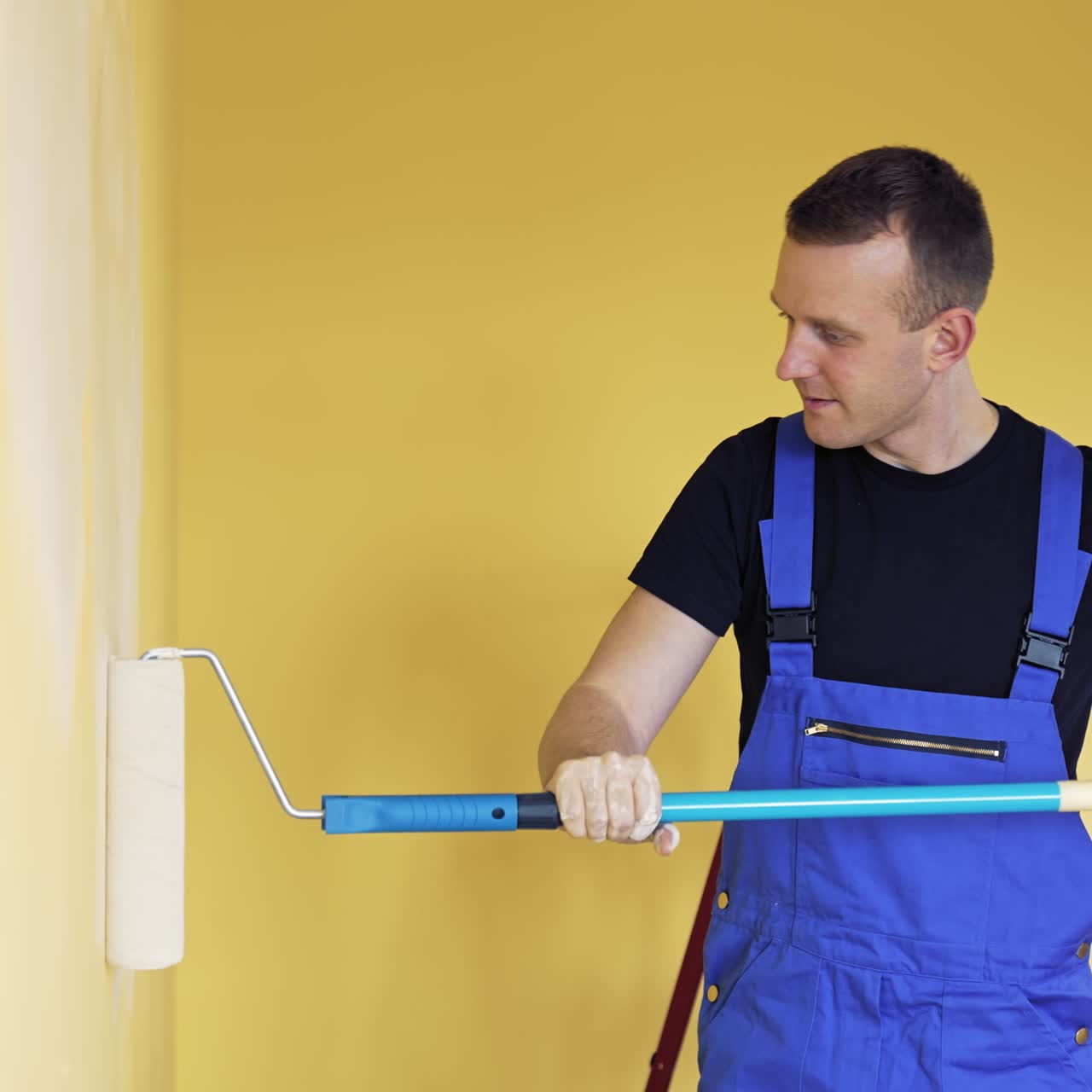 Operaio edile esperto con rullo per pittura. Giovane uomo che dipinge la parete con un rullo mentre ristruttura l'appartamento.