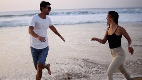 European-couple-is-running-on-the-beach.-Girl-jumps-into-her-boyfriend-arms,-he-whirling-her-at-beautiful-seaside.-Having-fun-together-at-vacation.-Slow-motion