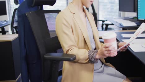 Biracial-businesswoman-drinking-coffee-and-holding-documents-in-office,-slow-motion