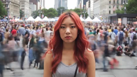 a woman with striking red hair calmly stands in the midst of a lively summer festival in new york city, as crowds move past her in a blur. the vibrant energy surrounds her.