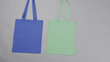 Close-up-of-blue-and-green-bags-on-grey-background,-with-copy-space,-slow-motion