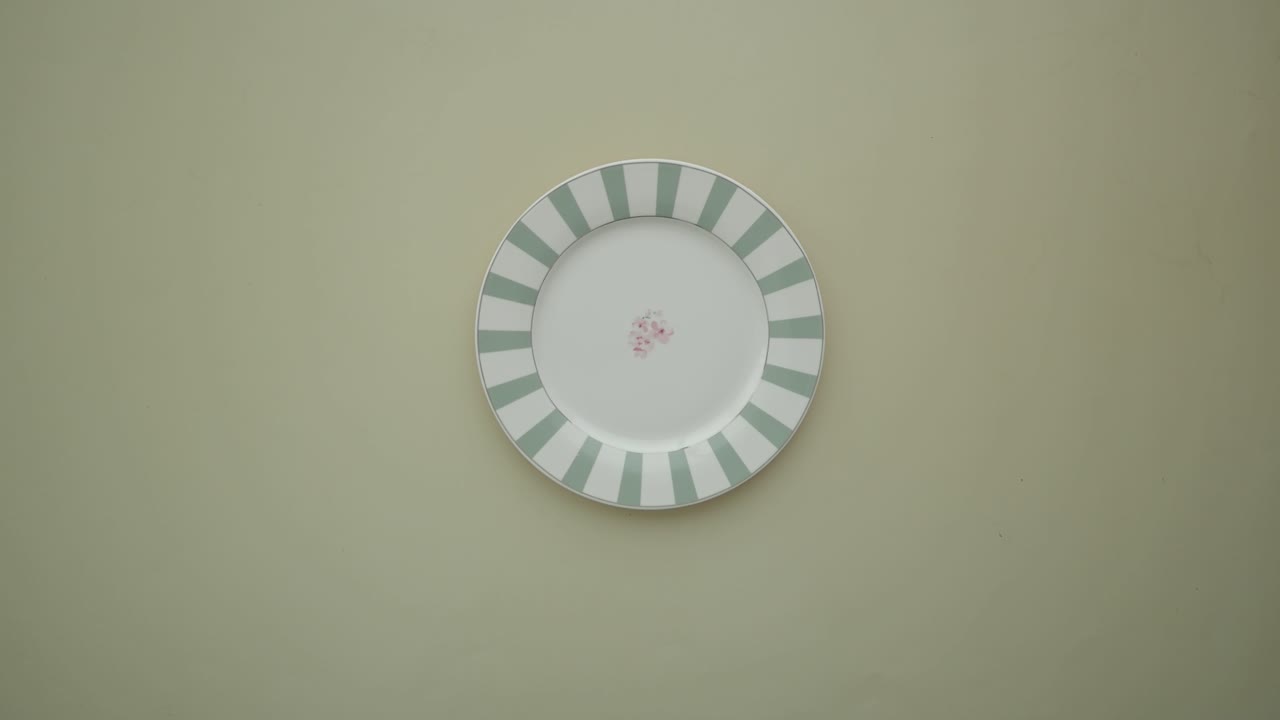 Hand Placing and Removing a Striped Plate on a Green Surface
