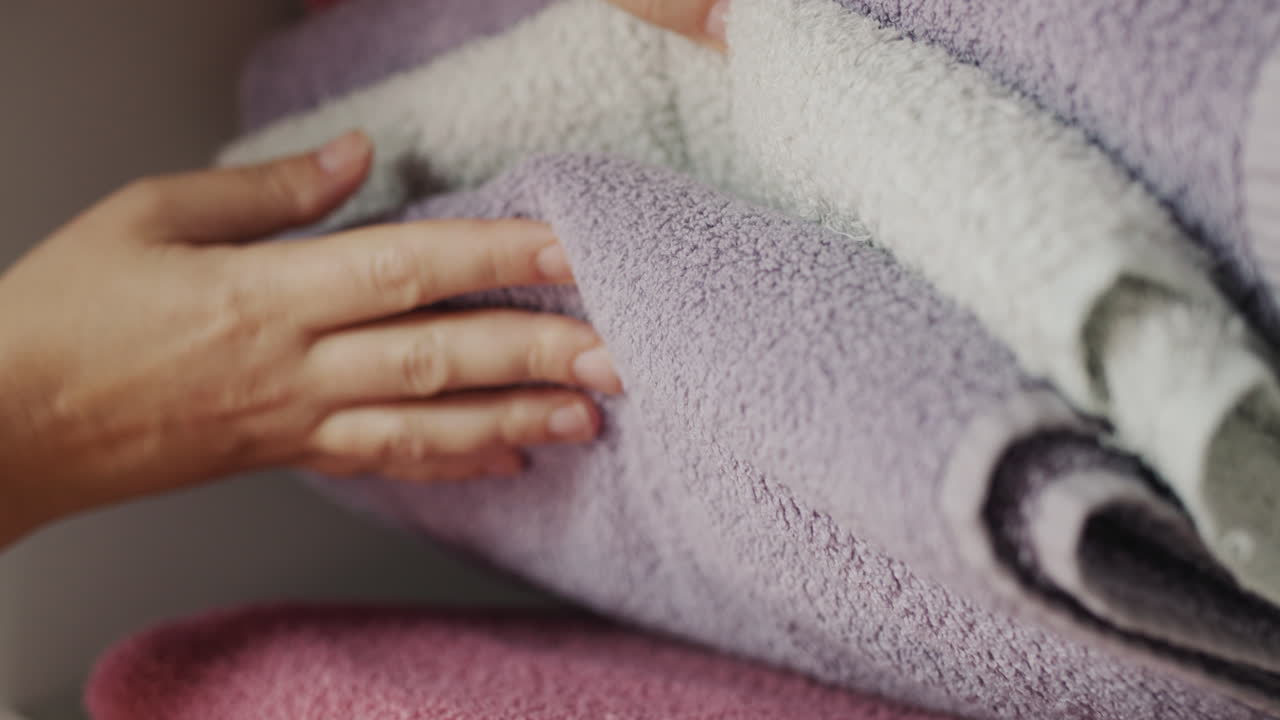 Women's fingers sort through clean towels on a shelf in the closet