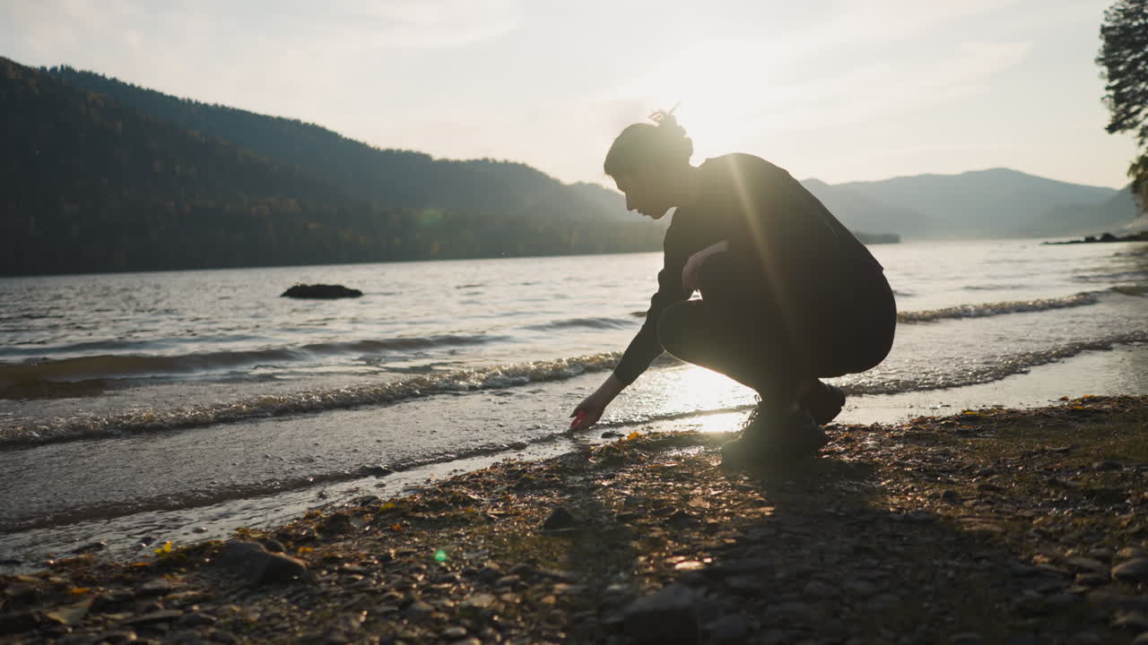 Woman stroking water of lake at back sunset. Attempt to relax and calm down from sadness of being alone on vacation. Connecting with nature at twilight