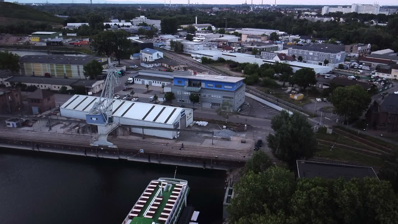 drone rising above cruise ship laying in the german harbour of the Rhine river while sun sets with docks and warehouses in view
