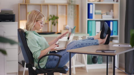 woman with feet on desk writes on laptop