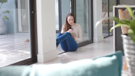 Mujer-Caucásica-Leyendo-Un-Libro-En-Una-Sala-De-Estar-Soleada,-Cámara-Lenta