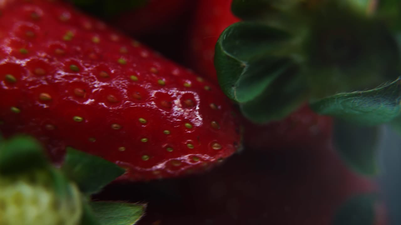 Makrodetaljert video av en gruppe jordbær, rødt jordbær, grønt blad, små frø, på et roterende refleksjonsstativ, jevn bevegelse.