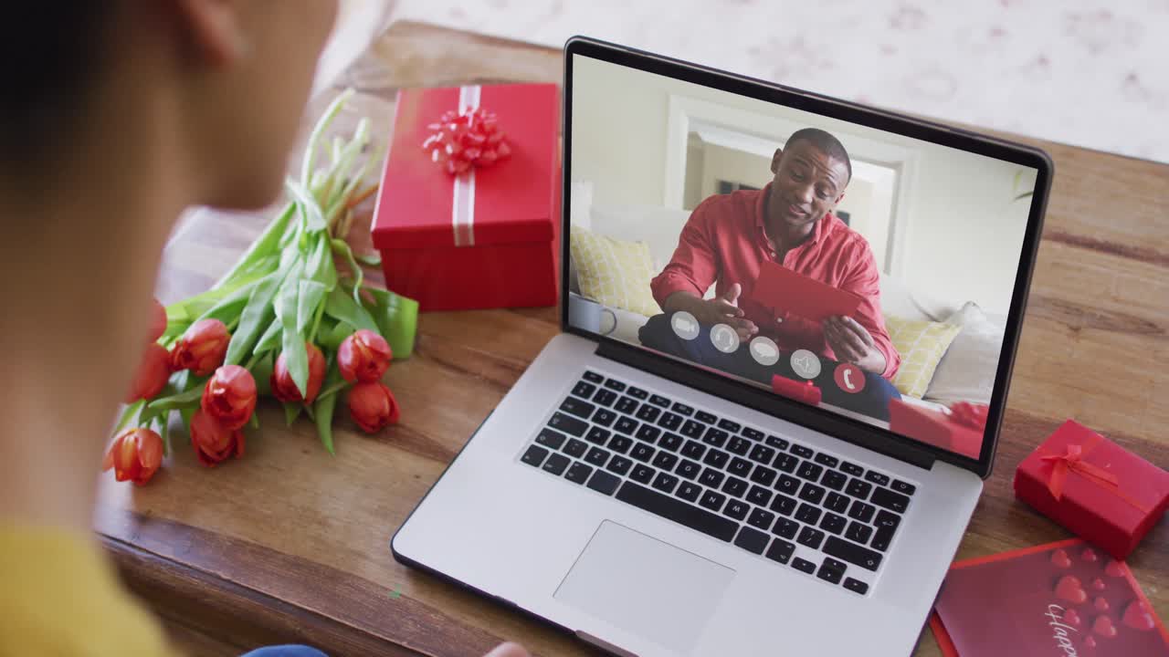 Happy african american man opening gift and making valentine's day video call on laptop