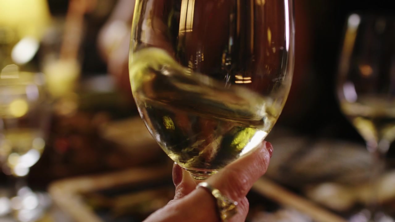 Mano che tiene un bicchiere di vino bianco a un'elegante tavola da pranzo, atmosfera festosa