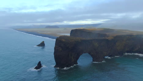 Aerial-cinematic-drone-pan-up-stunning-sunrise-fog-early-winter-at-Black-Sand-Beach-Apostles-fire-and-ice-ocean-next-to-Dyhrolaey-lighthouse-and-cave-Reynisfjara-Iceland
