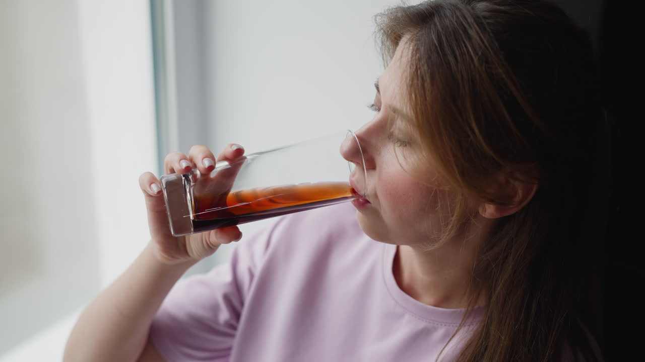 overhead view young white lady near glass window holding wine glass thoughtfully looking outside calm expression natural daylight softly illuminating face