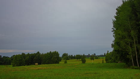 Storm-clouds-spread-across-open-sky-glowing-and-bright,-open-field-and-forest-hill