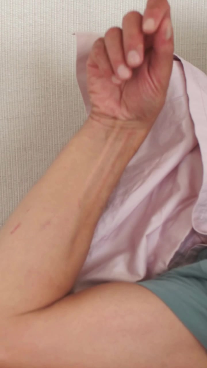 Video vertical: Hombre con camiseta turquesa levantando la mano cerca de la cara, bajando el antebrazo sobre la cama con sábana rosa.