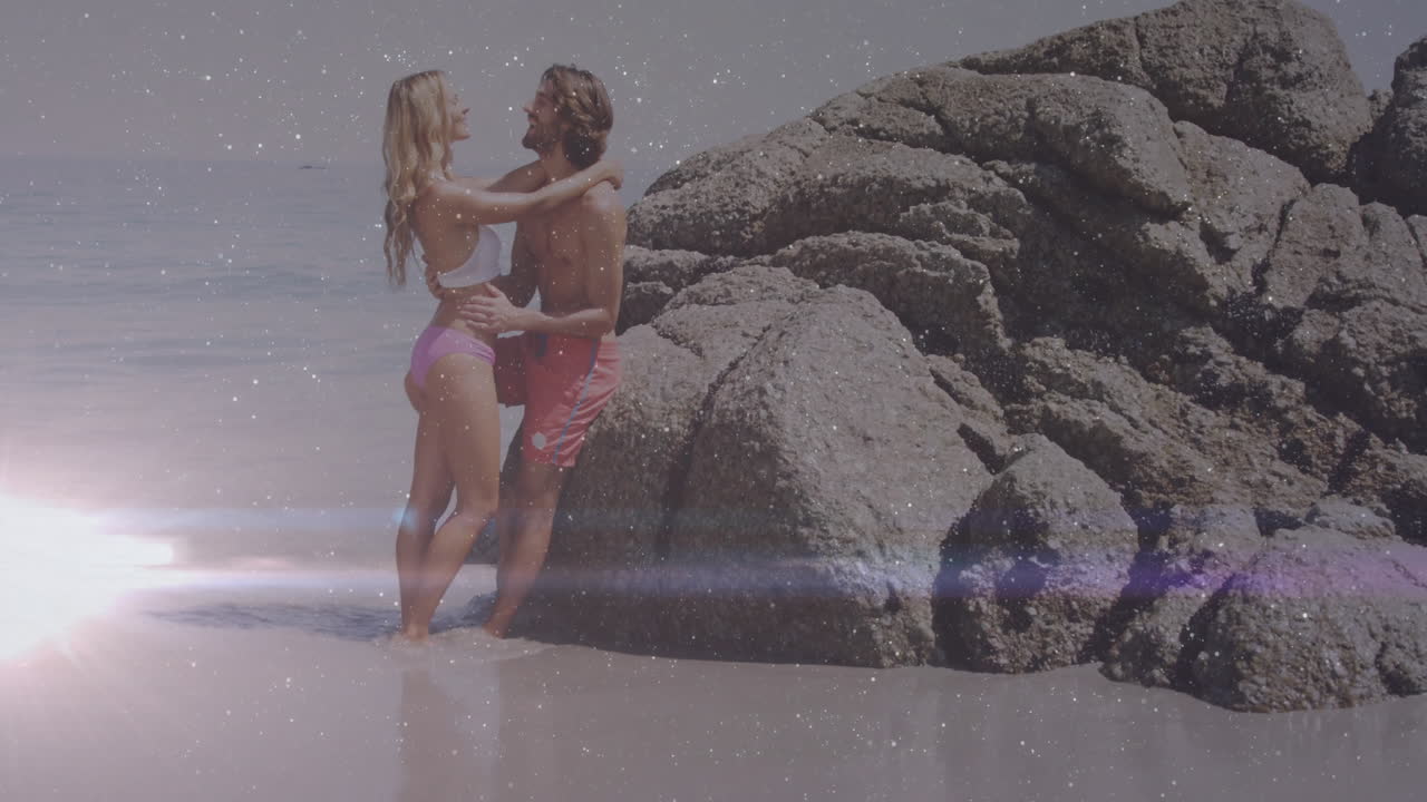 Man and woman embracing in shallow water, featuring lens flare sparkly light for travel marketing
