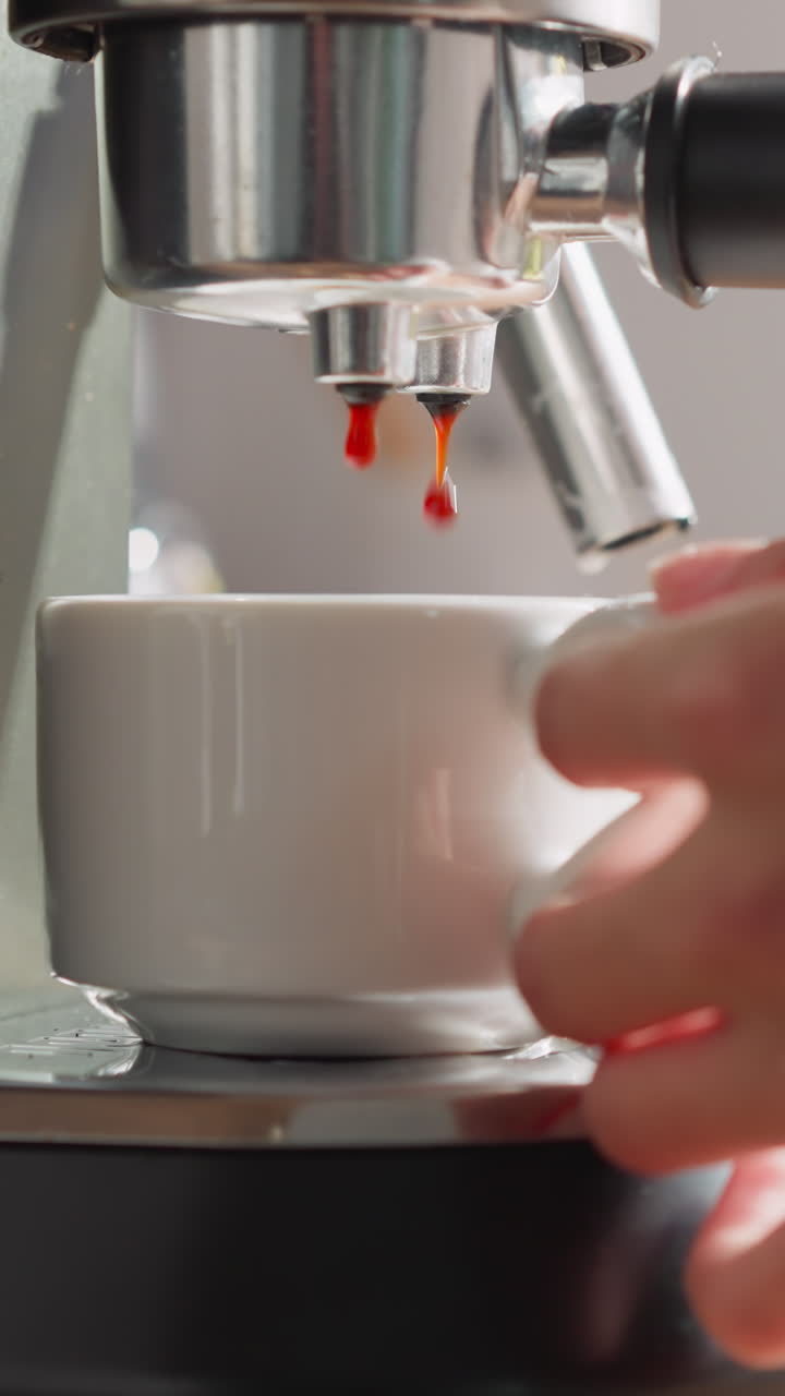 Brewed coffee drips from machine into cup closeup. Woman in bathrobe waits filling mug with hot coffee from coffeemaker in kitchen. Concept of morning ritual