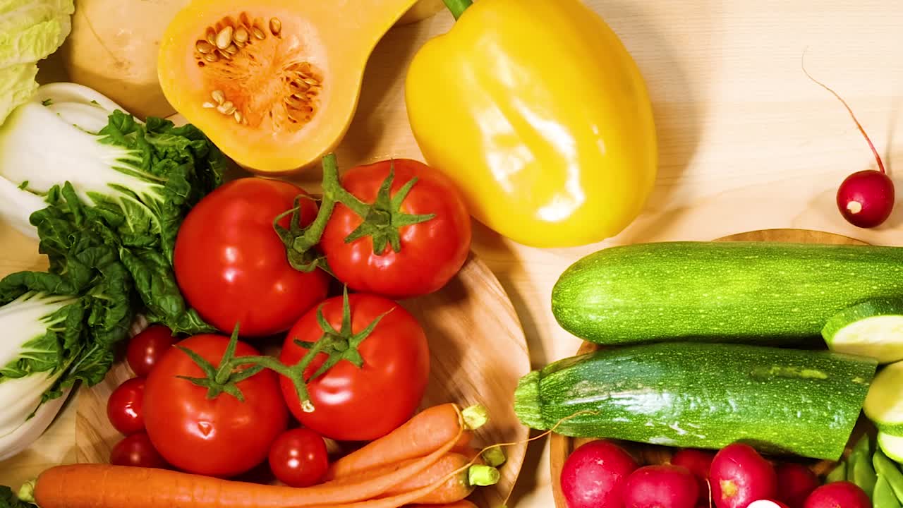 Um arranjo vibrante, visto de cima, de tomates, pimentões, abobrinhas e abóboras sobre uma mesa de madeira clara