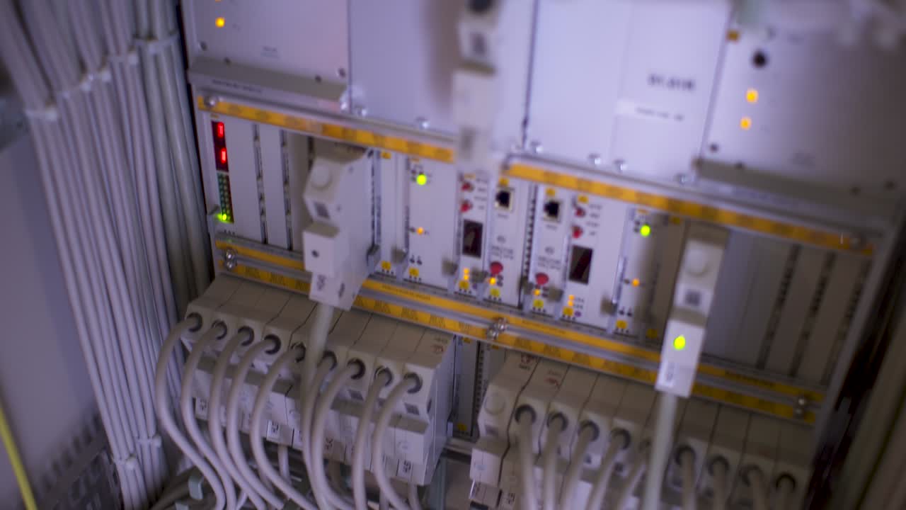 primer plano de un panel de control eléctrico gris en un entorno industrial, repleto de cables blancos y grises, interruptores y botones, algunos iluminados con luces amarillas y verdes