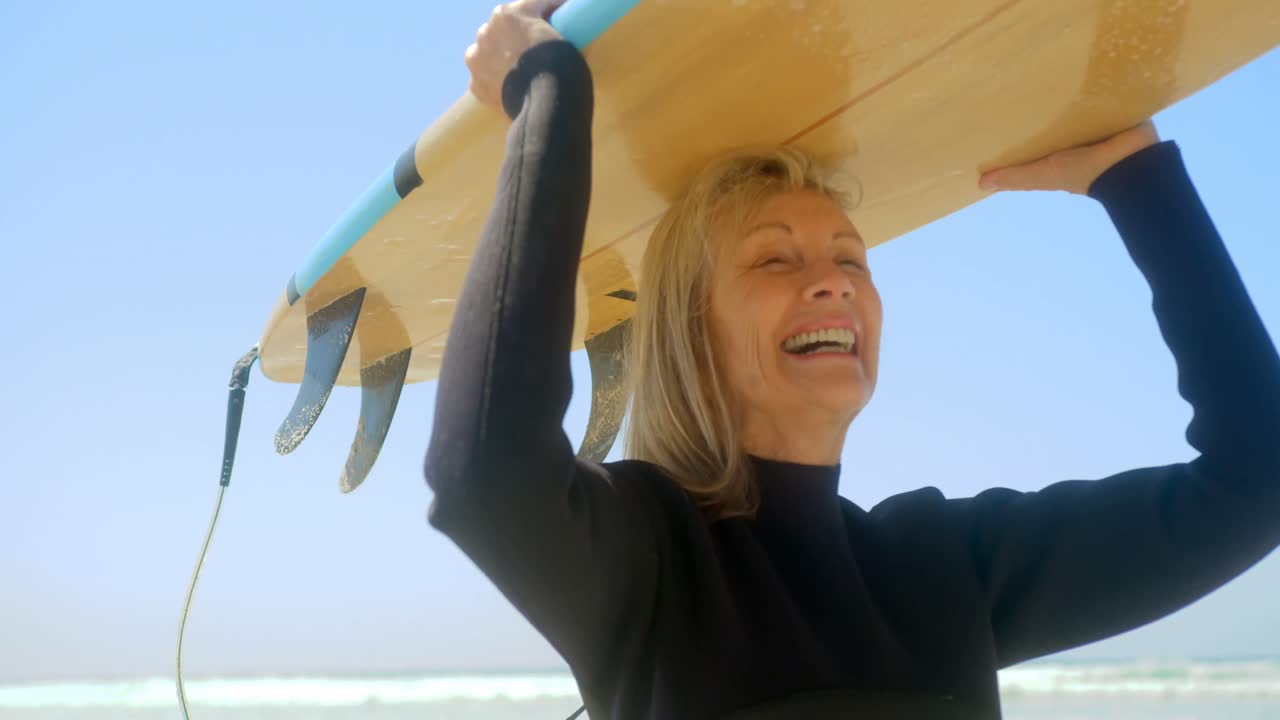 vista frontal de una surfista caucásica activa llevando una tabla de surf en la cabeza en la playa 4k