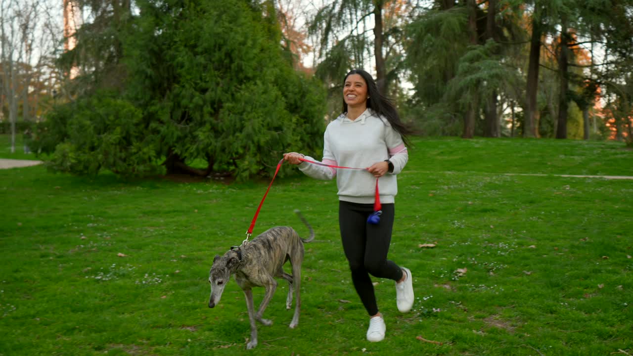 Donna felice che fa jogging con il suo levriero in un parco verde