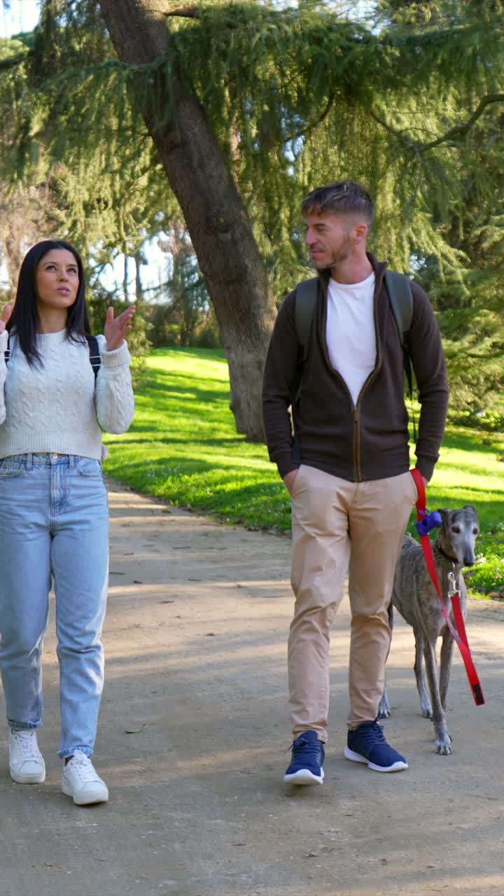 Pareja paseando a su perro galgo y conversando en un parque soleado