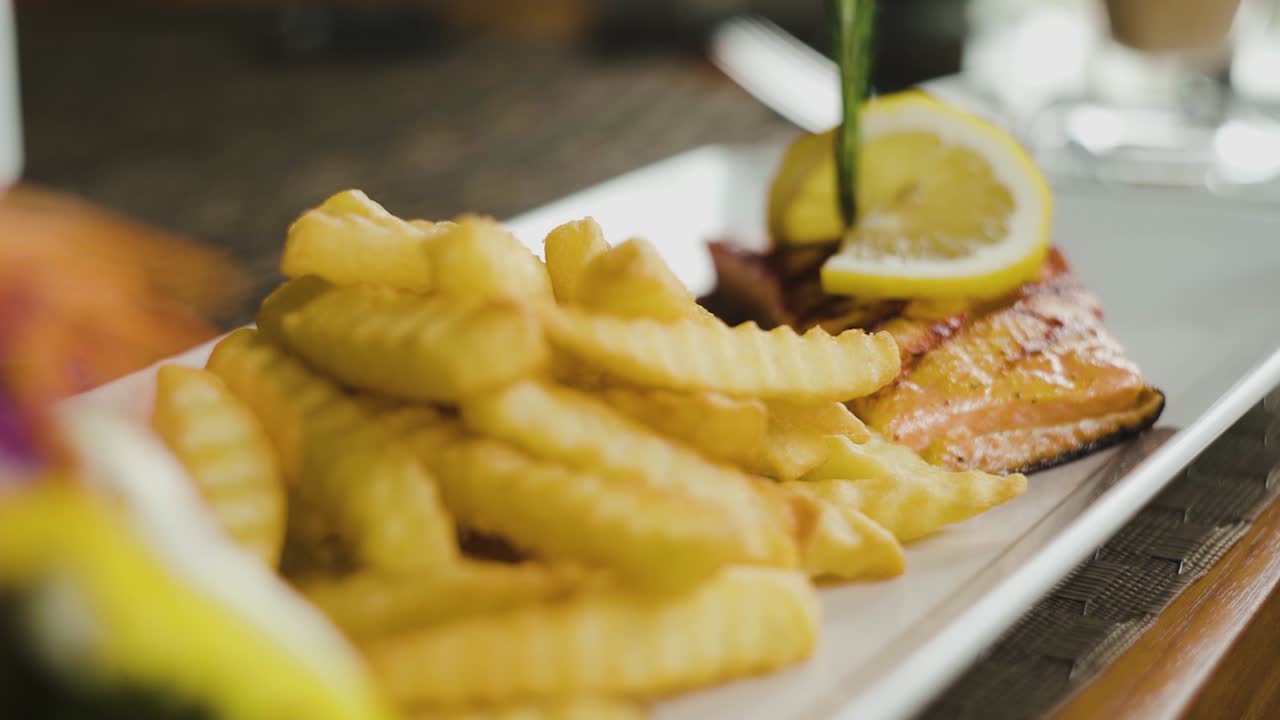 Trancio di salmone con patatine fritte e insalata di contorno, inquadratura statica ravvicinata con zoom lento