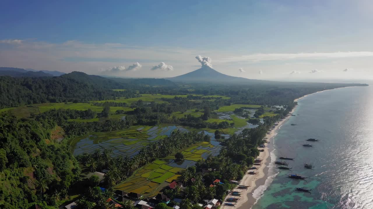 Aerial video captures a scenic coastal landscape with lush greenery, rice fields, and a distant