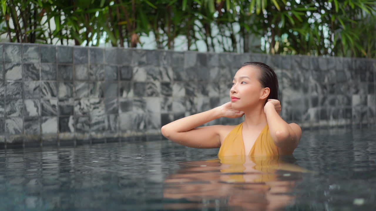 Medium close of a young, fit, healthy, attractive woman in a resort swimming pool pushing her wet hair back away from her face.Copy space