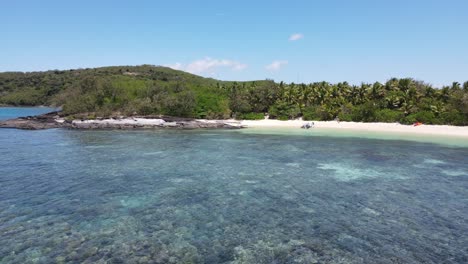 4K-drone-view-of-a-tropical-island-beachfront,-palm-trees-and-coral-reef-at-high-tide