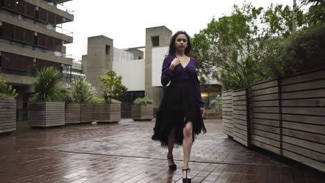 Young-attractive-woman-walking-through-windy-and-rainy-weather-around-plants-with-heels