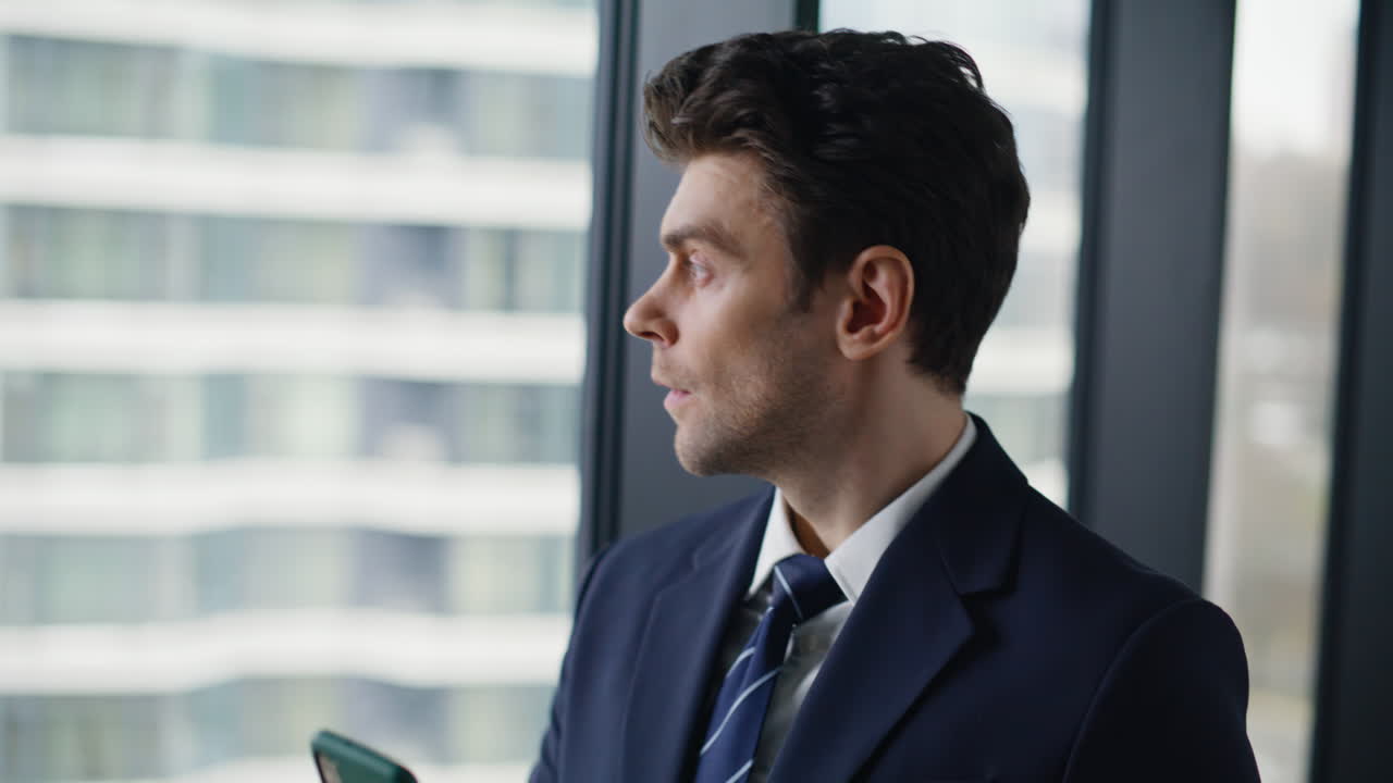 Wealthy businessman texting mobile phone standing by office window closeup