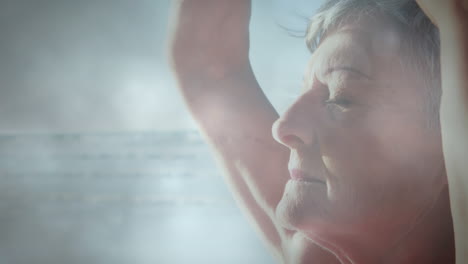 animation of glowing light over portrait of happy senior man practicing yoga by seaside