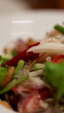 una colorida ensalada tailandesa con verduras frescas, chile y fideos, capturada en primer plano con una iluminación suave