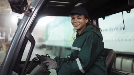 Potrait-of-an-African-American-woman-in-a-special-green-uniform-sitting-behind-the-wheel-of-a-truck-in-a-waste-processing-plant.-Processing-of-raw-materials,-recycling.-Pollution-control