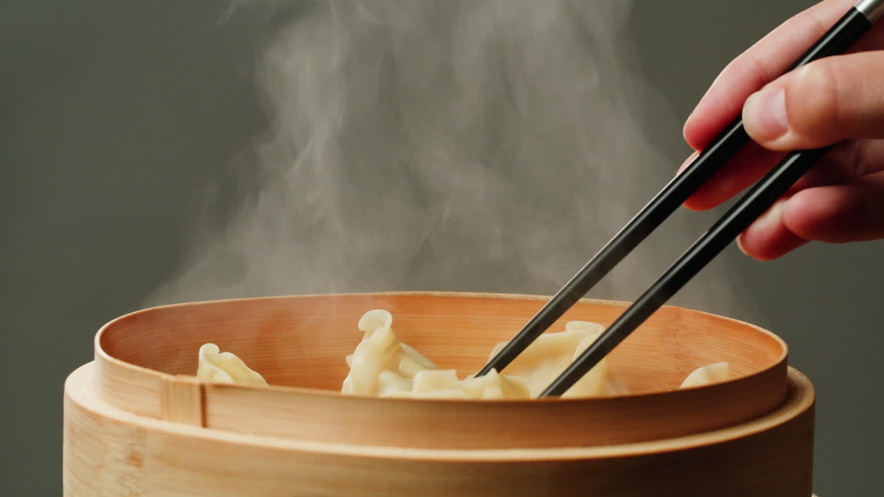 Bacchette che prendono un raviolo fumante da una vaporiera di bambù